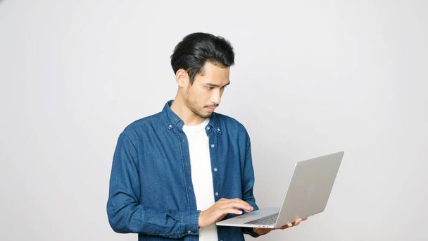 Jeune homme asiatique tenant ordinateur portable debout sur fond gris isolé, les gens et la technologie - Photo, image