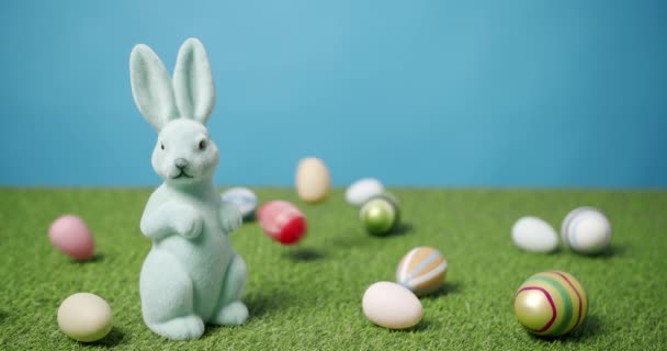 Rabbit Toy on a Blue Background of Green Grass with many colored eggs, Text. - Footage, Video