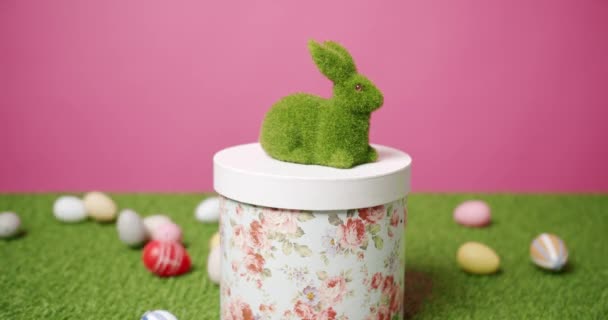 Rabbit Toy on a Pink Background of Green Grass with many colored eggs, Text. - Footage, Video