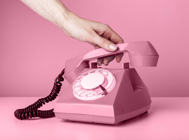 Woman hand holding retro phone handset on pink background and answering to call or hanging up. - Фото, зображення