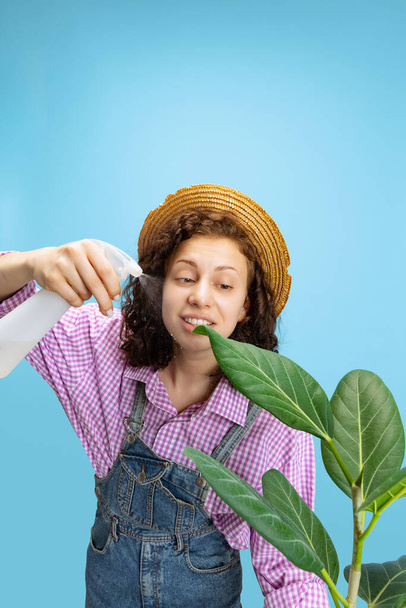 Portrait of young pretty girl, female gardener in work uniform watering flower isolated on white background. Concept of job, emotions, agronomy - 写真・画像