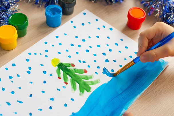 A child draws a Christmas tree. Ideas for drawing with bright colors. Drawing children on a white background. A little girl draws with paint and brushes. The concept of children's development - Photo, Image
