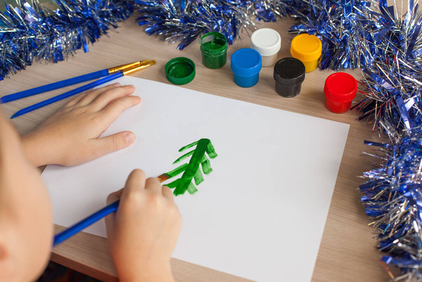 Les mains de l'enfant tiennent un pinceau pour le dessin et ramasse la gouache d'une boîte. Loisirs et animations pour enfants. Gros plan
. - Photo, image