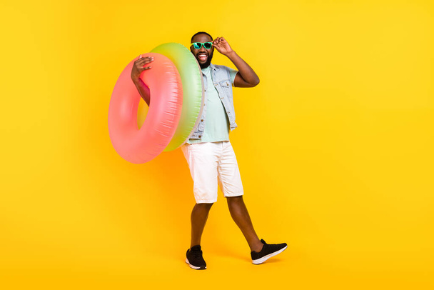 Full length body size view of attractive crazy cheery guy carrying rubber circle isolated over bright yellow color background - Фото, изображение
