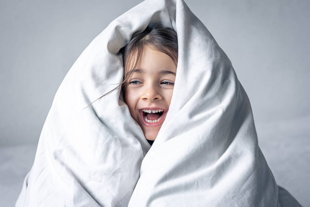 Slaperig klein meisje verpakt in een witte deken. - Foto, afbeelding