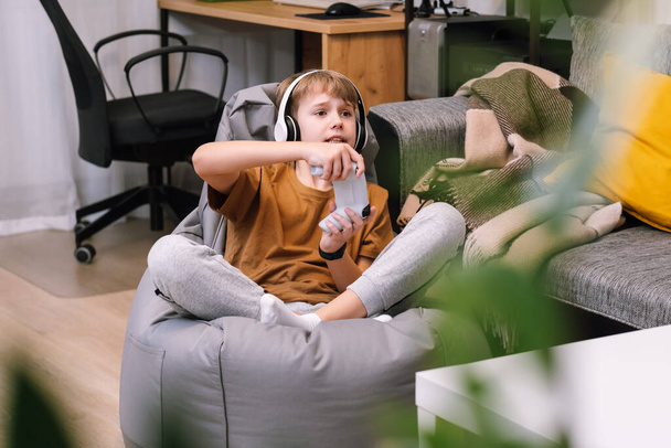Αγόρι έφηβος παίζει βιντεοπαιχνίδι με joystick κάθεται σε frameless καρέκλα beanbag - Φωτογραφία, εικόνα