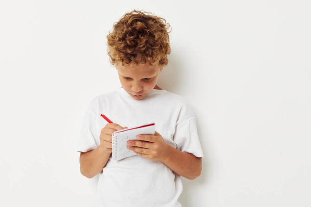 a boy in a white t-shirt draws with a pencil in a notebook - Фото, зображення