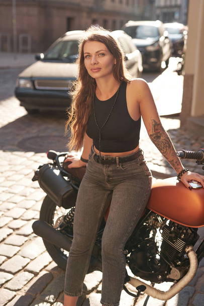Ruskeatukkainen nainen poseeraa kaupunkien retro moottoripyörä kujalla - Valokuva, kuva