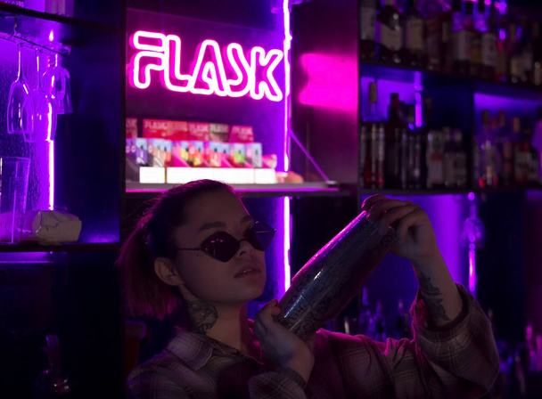 Woman bartender with cocktail shaker in nightclub bar with red pink and violet purple neon light, barman at club party - Foto, imagen