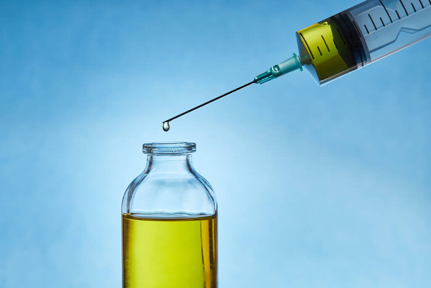A drop of liquid drips from the needle of a medical syringe into the bottle. - 写真・画像