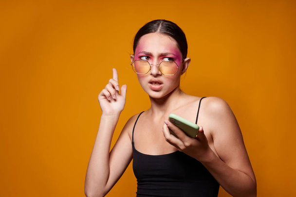 Mladá krásná žena s telefonem v ruce světlé make-up představovat módní emoce žluté pozadí beze změny - Fotografie, Obrázek