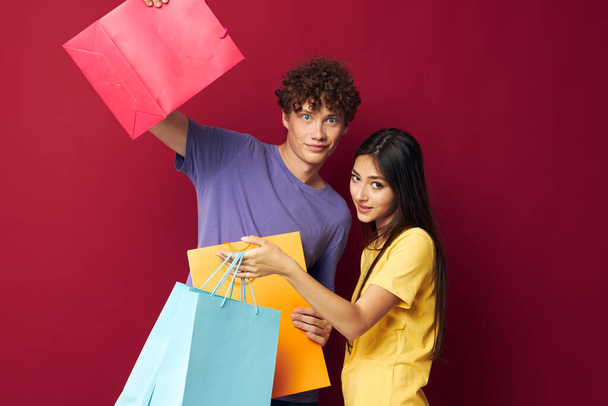 retrato de un hombre y una mujer coloridas bolsas de compras divertido fondo rojo inalterado - Foto, Imagen