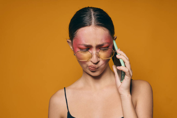 Junge schöne Frau mit Brille helles Make-up posiert schwarzen Jersey am Telefon sprechen isolierten Hintergrund unverändert - Foto, Bild