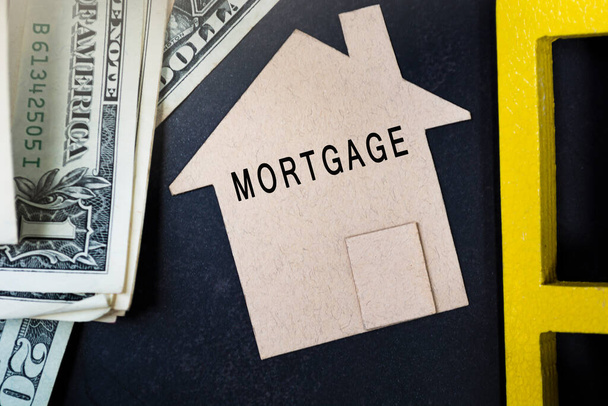 Hypothekentext auf braunem Papierhausmodell mit Dollarnoten auf dunklem Holztisch. Konzept für Darlehen, Hypothek und Refinanzierung. - Foto, Bild