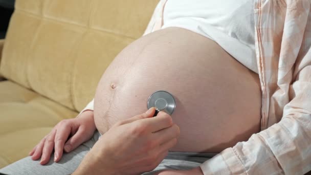 tunnistamaton mies kuuntelee vauvaa raskaana olevan naisen vatsassa fonendoskoopilla - Materiaali, video