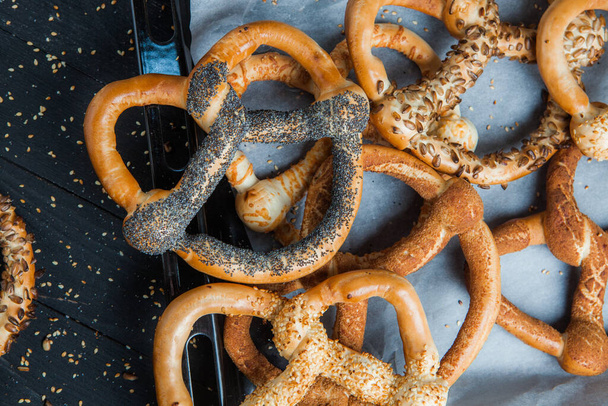 Fresh prepared homemade soft pretzels. Different types of baked bagels with seeds on a black background. - Photo, image