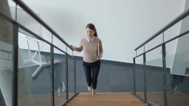 Милая молодая деловая женщина, идущая по служебной лестнице и держащая ноутбук - Кадры, видео
