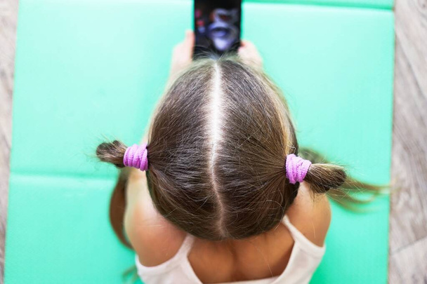 girl child with pigtails talking on the phone, getting homework on a cellular connection, during isolation and a pandemic, a convenient means of communication - Foto, Bild