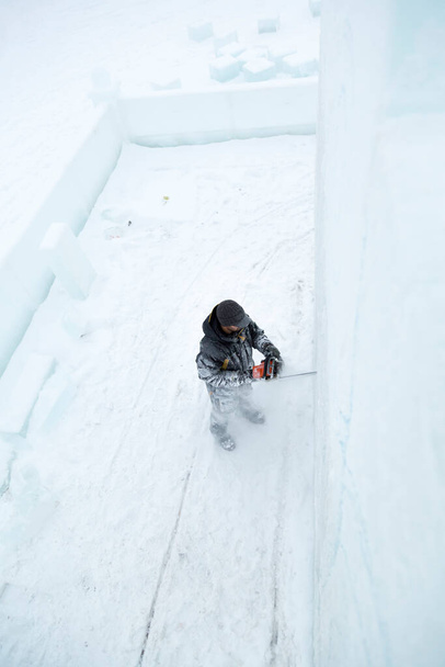 De beeldhouwer snijdt de contouren van de toekomstige compositie uit met een kettingzaag in een ijsplaat - Foto, afbeelding