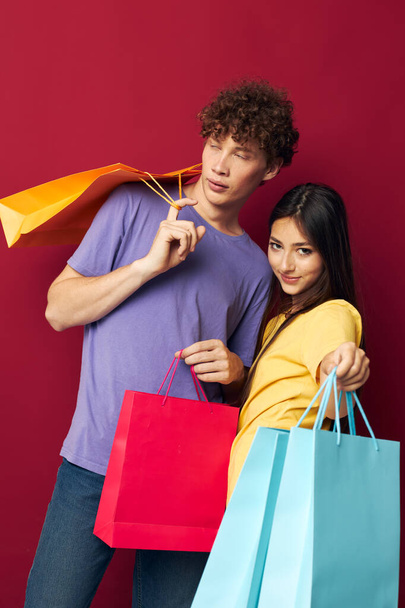 portrait of a man and a woman in colorful T-shirts with bags Shopping red background unaltered - Fotografie, Obrázek
