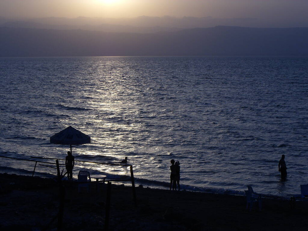 Мертве море (Йорданія, 9 серпня 2010 року). Кілька людей відпочивають під час заходу сонця на тихому пляжі на узбережжі Мертвого моря в Йорданії. - Фото, зображення