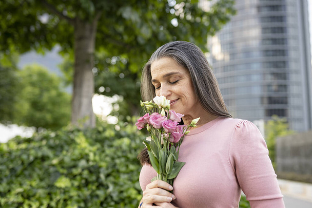 senior vrouw, ruiken wat bloemen in de stad - Foto, afbeelding