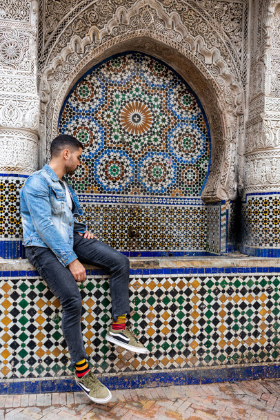 Moroccan man sitting next to an outdoor ceramic tiles fountain in the old medina of Fes - Fotoğraf, Görsel