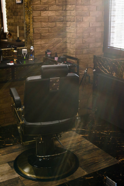 Fekete bőrfotel egy borbélyüzletben a napon. Modern fodrászat és fodrászat, fodrászat férfiaknak Barbershop fotel. - Fotó, kép