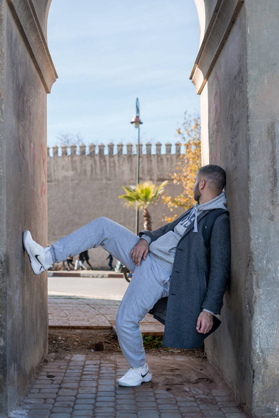 Moroccan man leaning against a wall wearing stylish grey coat and white Nike shoes - Photo, Image