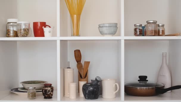 Kitchen utensils and tableware on white shelves. Well organized kitchen concept. Modern interior. Open cupboard with clean dishes. - Footage, Video