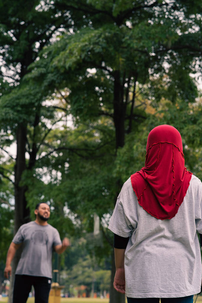 Familia asiática jugando bádminton en el parque. Mujer en hijab, vista desde atrás. - Foto, imagen