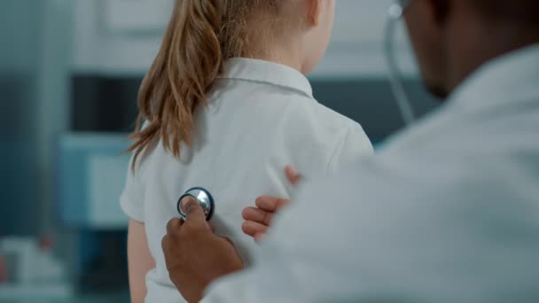 Médico afroamericano consultando a un niño pequeño con estetoscopio - Metraje, vídeo