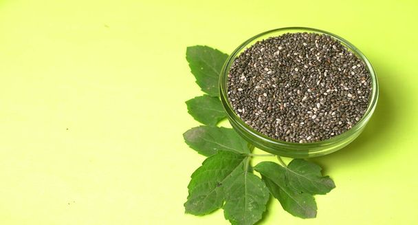 Schüssel schwarzer Sesamsamen mit grünen Blättern, gesundes Ernährungskonzept  - Foto, Bild