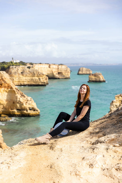 young beautiful girl in sits on a rock against the backdrop of the beach and the ocean in Portugal - Foto, Imagen