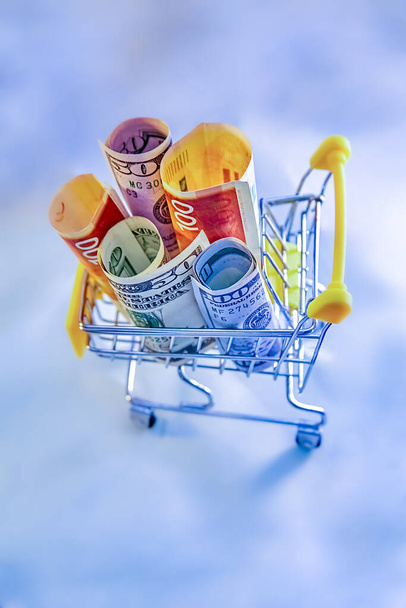 concept - Shopping Cart Trolleys with money, dollars and Israeli new shekels on light background - Φωτογραφία, εικόνα