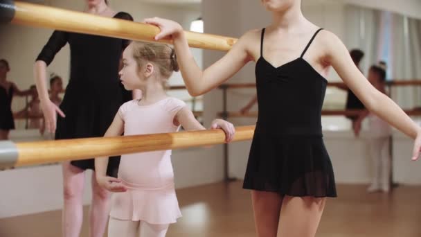 Pequeña bailarina modesta entrenando en el estudio cerca del stand con su entrenador femenino - Imágenes, Vídeo