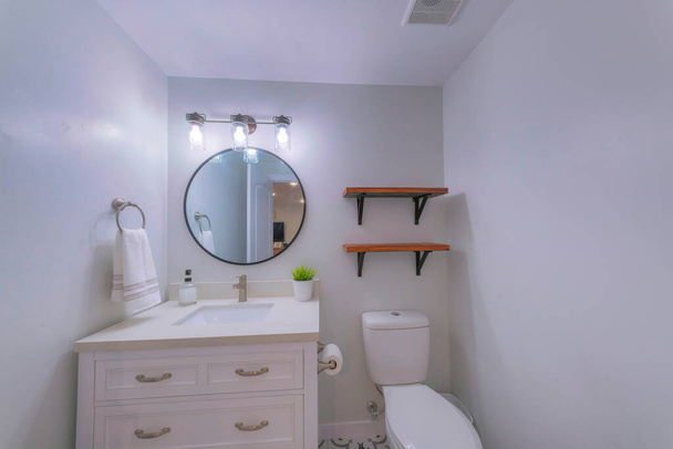 Kleines Badezimmer mit Holzregalen und gerahmtem ovalen Spiegel - Foto, Bild