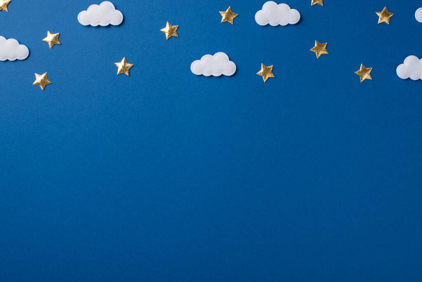 Foto de vista superior de los confeti dorados dispersos en forma de estrellas y confeti esponjoso suave en forma de nubes blancas en el agradable copyspace fondo aislado azul profundo - Foto, Imagen