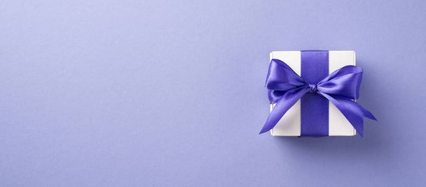 Foto vista superior de la composición del día de la mujer caja de regalo blanca con arco violeta sobre fondo púrpura pastel aislado con espacio vacío - Foto, Imagen