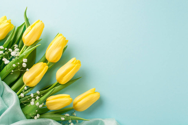 Foto vista superior de la composición del día de la mujer manojo de tulipanes amarillos gypsophila blanco y textil suave sobre fondo azul pastel aislado con copyspace - Foto, Imagen