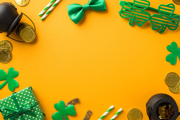 Top view photo of st patrick's day decor clover shaped party glasses straws green bow-tie giftbox horseshoe shamrocks pots with gold coins on isolated yellow background with blank space in the middle - Photo, Image