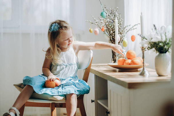 Paskalya tatili için hazırlık. Küçük bir kız tatil beklentisiyle elinde meyvelerle bir odada bir sandalyede oturuyor. Aile gelenekleri, aile değerleri. - Fotoğraf, Görsel
