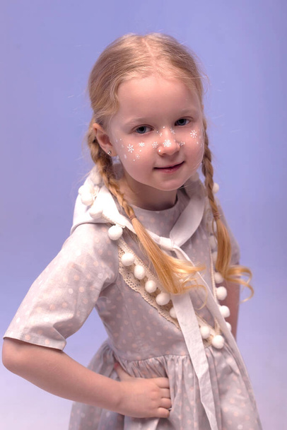 Een klein mooi en lief meisje in een stijlvol feestelijke jurk en met een dwerghoed in een wit interieur. Foto met selectieve focus en tintje.Het kind lacht en kijkt naar de camera. - Foto, afbeelding