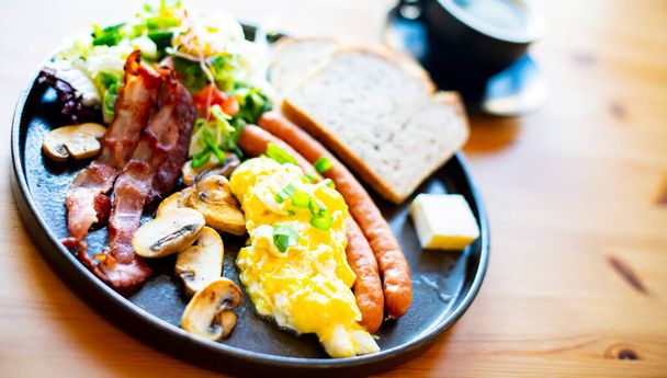 Breakfast with scrambled eggs, bacon, sausages and toast on a restaurant table - Foto, Bild