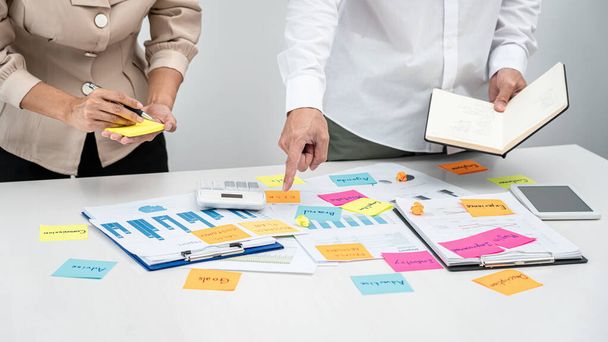 Business people team, boss holding book and pointing data on the table to explaining about new business project while businesswoman writing keyword on post it notes while meeting together in office - Photo, image