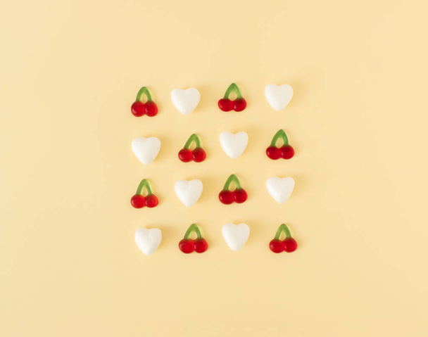 Creative spring idea made of white hearts and gummy cherry candies on pastel yellow background. MInimal Valentines day or spring concept. Top view, flat lay. - Photo, Image