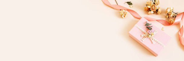 Caixa de presente rosa bonita com flores de rosas secas e fitas em fundo pastel. Presente para férias, aniversário, casamento, Dia das Mães, Dia dos Namorados, Dia das Mulheres. Espaço para cópia. Vista superior, deitado plano. Banner - Foto, Imagem