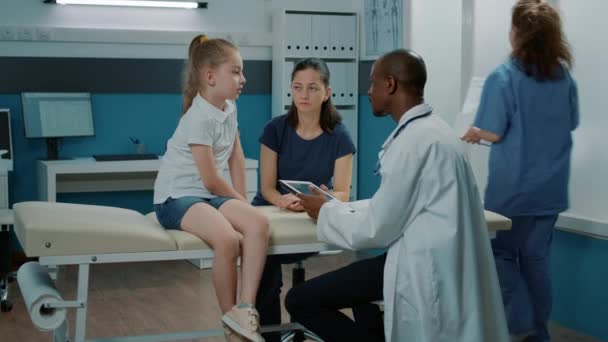Африканский американский медик делает заметки на планшете, чтобы проконсультироваться с ребенком - Кадры, видео