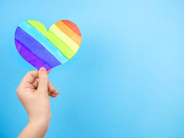 Female hand holding multicolored heart on blue background. Concept of love , LGBT - Foto, Imagen