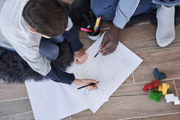 Multiracial father telling something to his son while he is drawing at the floor attentively - Photo, image